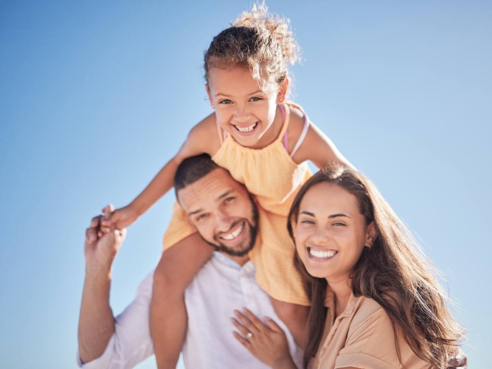 Happy diverse family thriving together - father carrying daughter on shoulders with mother smiling